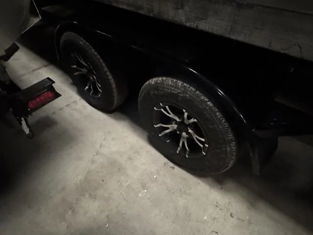 Slide: The Image of 2023 Manitou Explore 22 Max Bench trailer wheels in a dimly lit garage. - 25