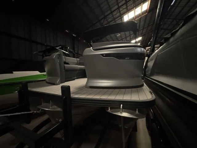 Slide: The Image of 2023 Manitou Explore 22 Max Bench pontoon boat in a dimly lit warehouse. - 4