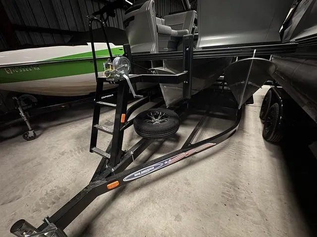 Slide: The Image of 2023 Manitou Explore 22 Max Bench boat on trailer in a dimly lit garage. - 6