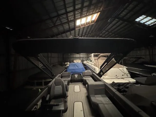 Slide: The Image of 2023 Manitou Explore 22 Max Bench boat in a dimly lit storage facility. - 7