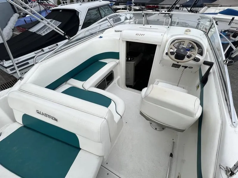 Slide: The Image of 2000 Glastron 249 boat interior with white and teal seating, steering wheel, and cabin entrance. - 10
