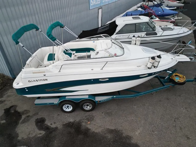 Slide: The Image of 2000 Glastron 249 boat on trailer, white and teal, parked near other boats. - 14