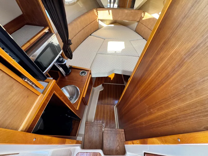 Slide: The Image of 2016 Cutwater C-28 cabin interior with wood finish, kitchenette, and cozy sleeping area. - 6