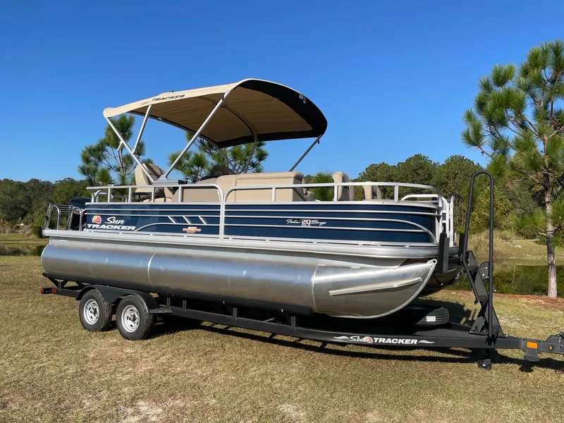 Slide: The Image of 2025 Sun Tracker Fishin' Barge 20 DLX pontoon boat on trailer, parked outdoors. - 2