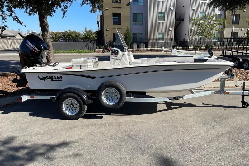 The Image of 2025 Mako Pro Skiff 15 CC boat on trailer, parked outdoors near modern buildings. - 0