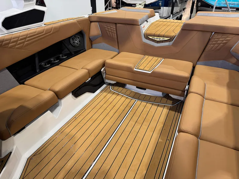Slide: The Image of 2025 Nautique Super Air Nautique S23 interior with tan seating and wood-style flooring. - 15