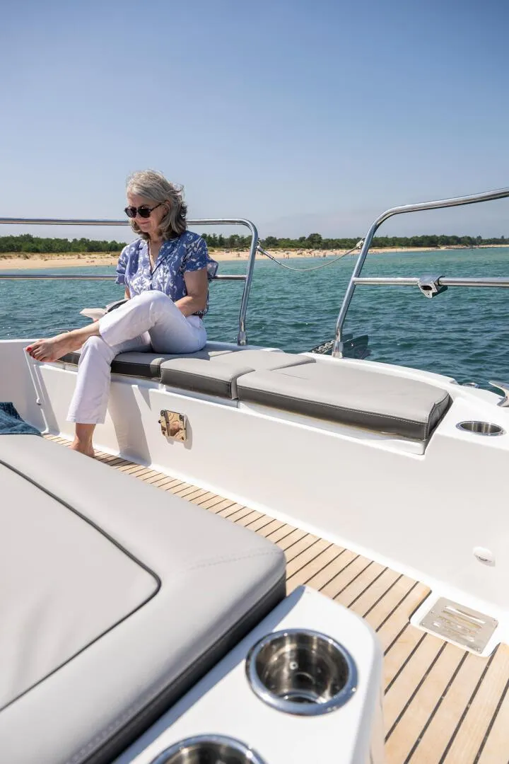 Slide: The Image of Woman relaxing on Jeanneau NC 1295 Coupe yacht, 2025 model, near scenic coastline. - 13