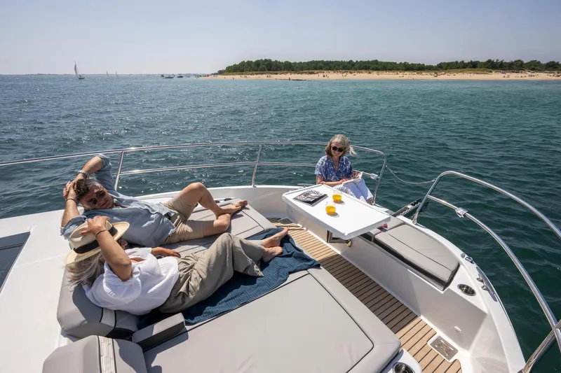 Slide: The Image of 2025 Jeanneau NC 1295 Coupe yacht with people relaxing on deck, ocean view. - 14