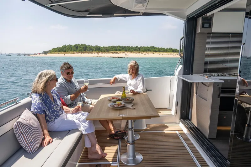 Slide: The Image of 2025 Jeanneau NC 1295 Coupe with people enjoying a meal on deck. - 15