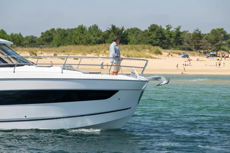 Slide: The Image of 2025 Jeanneau NC 1295 Coupe cruising near a sandy beach with lush greenery. - 6