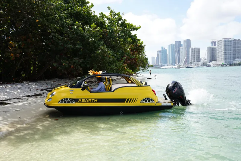Slide: The Image of Yellow 2025 Car Off-shore Fiat 500 Abarth amphibious vehicle on beach near city skyline. - 13