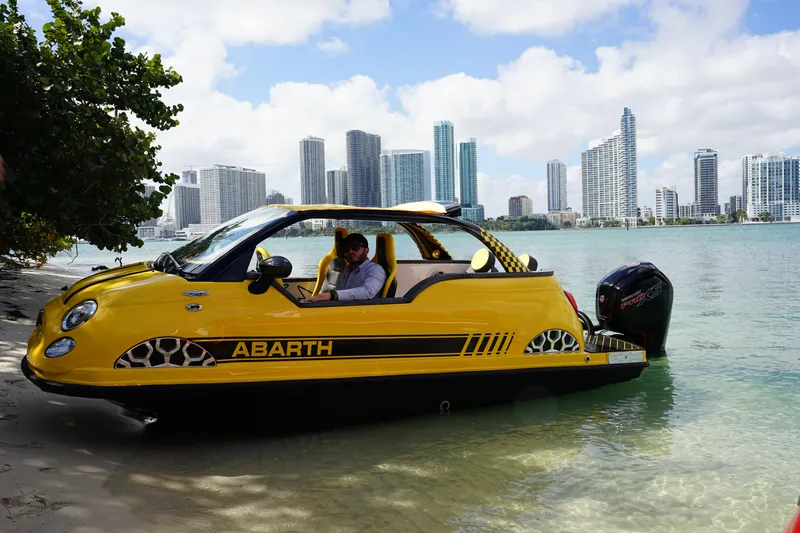 Slide: The Image of Yellow Car Off-shore Fiat 500 Abarth boat on water, city skyline in background, 2025 model. - 2