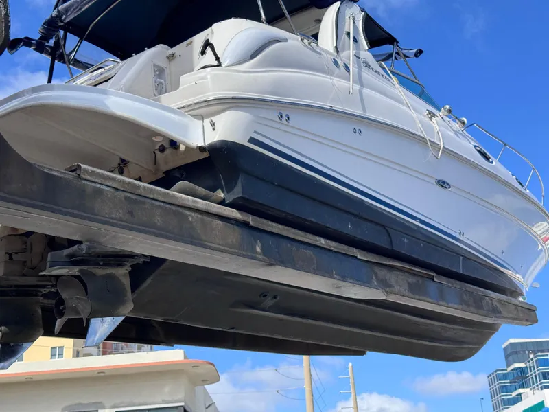 Slide: The Image of 2005 Sea Ray 280 Sundancer boat lifted, showcasing hull and design against blue sky. - 12