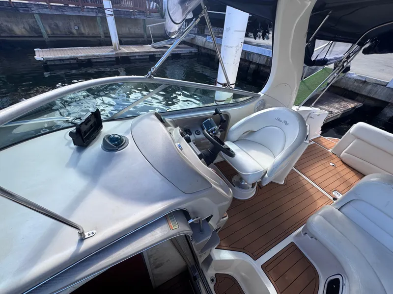 Slide: The Image of 2005 Sea Ray 280 Sundancer cockpit with steering wheel and seating, docked by the water. - 51