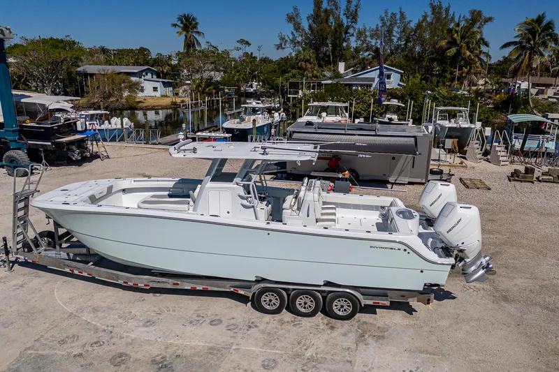 Slide: The Image of 2025 Invincible 33 Catamaran on trailer, parked in a marina with boats and trees. - 1