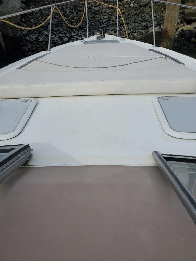 Slide: The Image of Larson 330 CABRIO 2000 boat deck with hatches and railing, docked near rocky shore. - 23