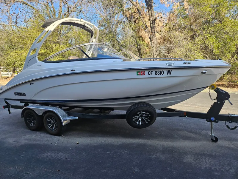 Slide: The Image of 2022 Yamaha Boats 212S on trailer, parked outdoors, surrounded by trees. - 7