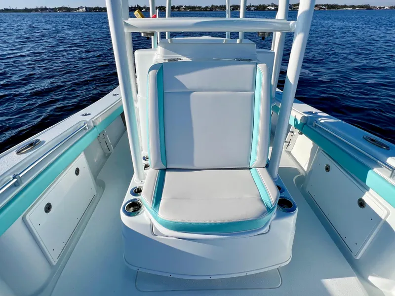 Slide: The Image of 2022 Yellowfin 26 Hybrid boat with cushioned seating, turquoise accents, and cup holders on calm water. - 33