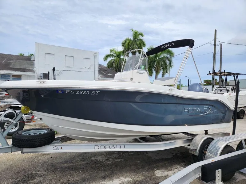 Slide: The Image of 2020 Robalo R180 boat on trailer, parked outdoors with palm trees in background. - 13
