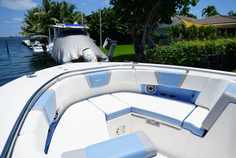 Slide: The Image of 2024 Robalo R360 boat interior with blue and white seating, docked near lush greenery. - 16