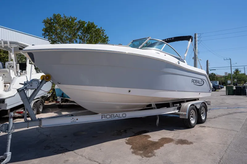 Slide: The Image of 2023 Robalo R227 boat on trailer, parked outdoors under clear blue sky. - 2