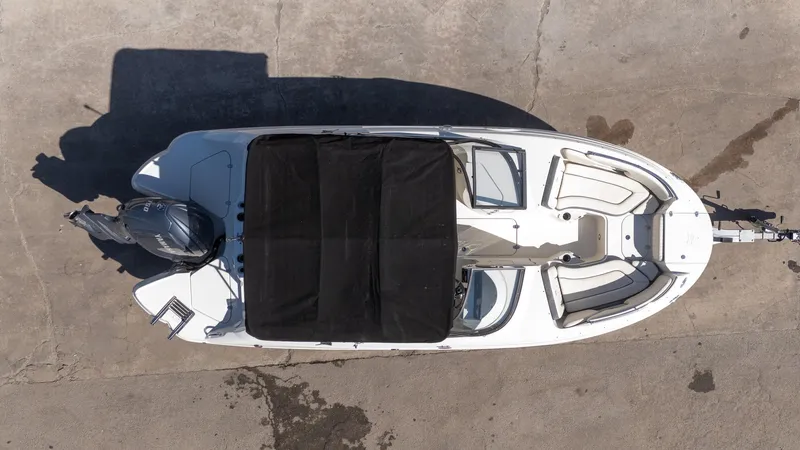 Slide: The Image of 2024 Stingray 211DC boat, aerial view, black cover, white interior, parked on concrete. - 20