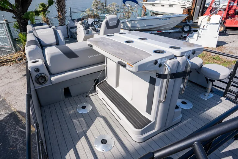 Slide: The Image of 2024 Sylvan L3 DLZ Bar pontoon boat with seating and bar area, docked outdoors. - 6