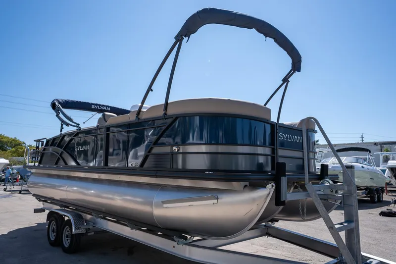 Slide: The Image of 2024 Sylvan L3 DLZ Bar pontoon boat on trailer under clear blue sky. - 1