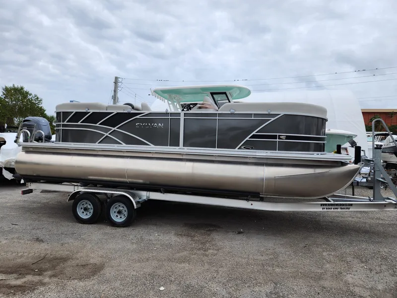 Slide: The Image of 2024 Sylvan 822 LZ pontoon boat on trailer, parked outdoors under cloudy sky. - 5
