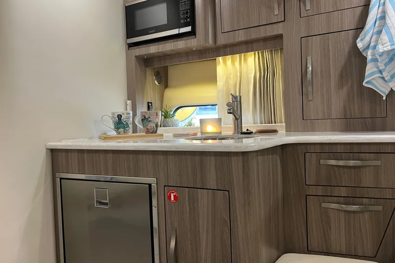 Slide: The Image of 2019 Regal 33 Express boat interior with kitchenette, featuring microwave, sink, and modern cabinetry. - 33