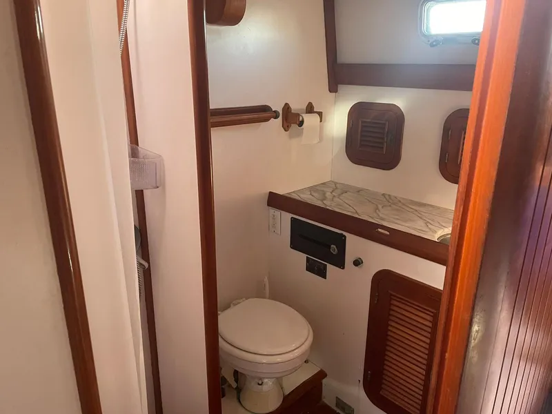 Slide: The Image of Compact boat bathroom with wooden accents, featuring a toilet and small window, Passport 51, 1987 model. - 68