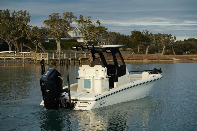 Slide: The Image of 2025 Scout 261 XSS boat cruising on a calm waterway near a wooded shoreline. - 1