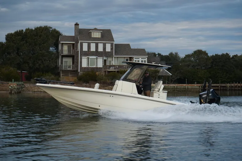 Slide: The Image of 2025 Scout 261 XSS boat cruising on a calm lake near a lakeside house. - 19