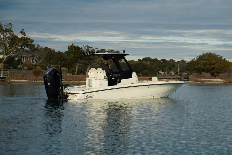 Slide: The Image of 2025 Scout 261 XSS boat on calm water, side view, with trees in the background. - 2