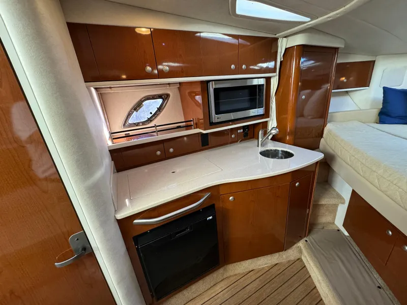 Slide: The Image of 2008 Sea Ray 310 Sundancer interior with kitchenette, featuring wood cabinets, sink, and microwave. - 12