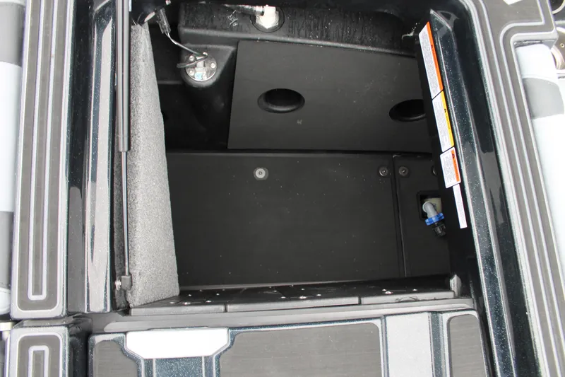 Slide: The Image of Storage compartment of 2025 Malibu 23 MXZ boat, featuring black interior and safety labels. - 14
