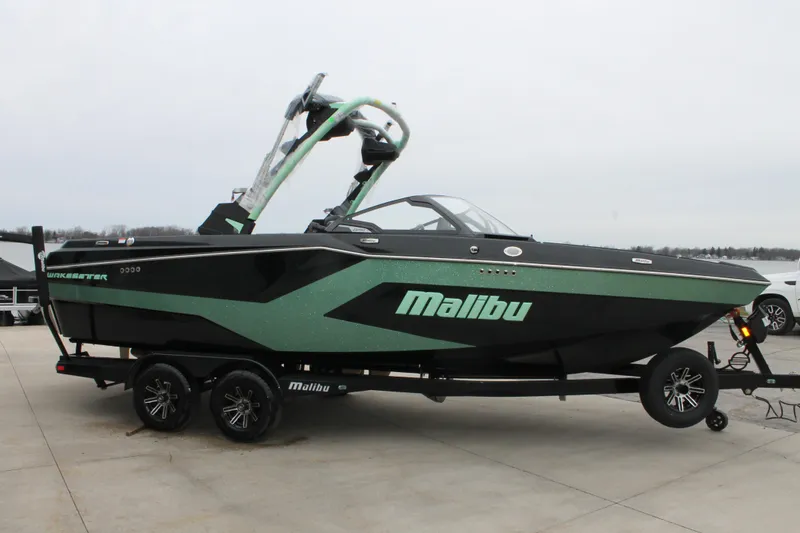 Slide: The Image of 2025 Malibu 23 MXZ boat on trailer, black and green design, side view. - 2