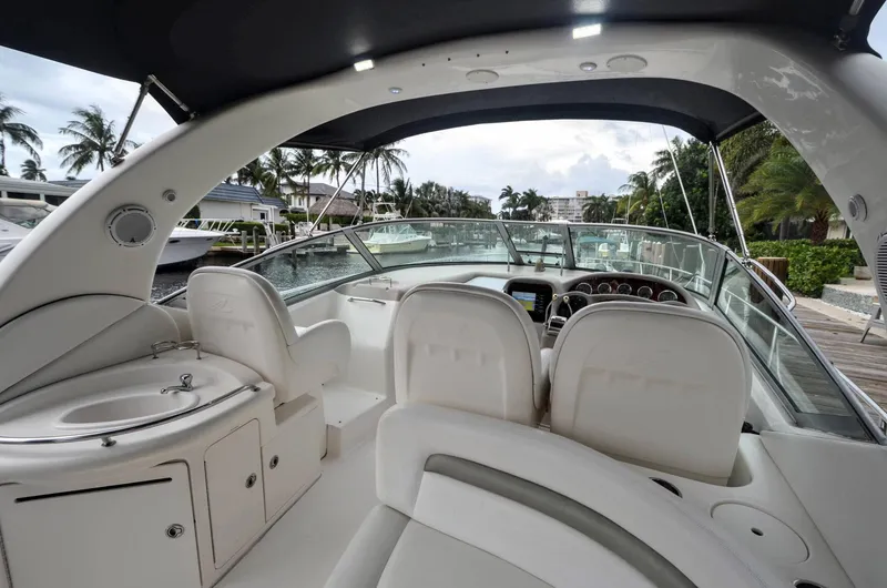 Slide: The Image of 2007 Sea Ray 340 Sundancer cockpit with helm, seating, and sink, docked near palm trees. - 24