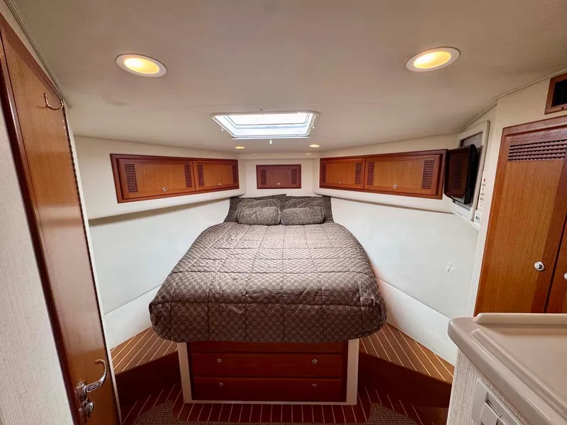 Slide: The Image of 2002 Cabo 47 Flybridge Sportfisher cabin with bed, wooden cabinets, and overhead lighting. - 21