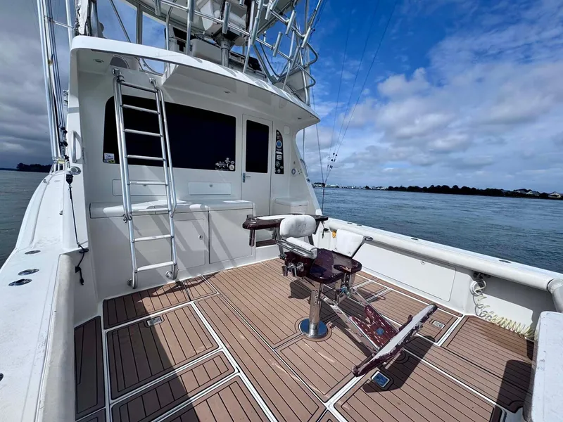 Slide: The Image of 2002 Cabo 47 Flybridge Sportfisher boat deck with fishing chair and ladder, under blue sky. - 36