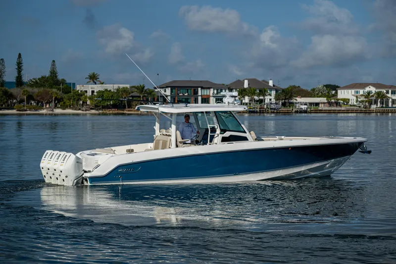 Slide: The Image of 2024 Boston Whaler 380 Outrage boat cruising on calm waters near a coastal neighborhood. - 19