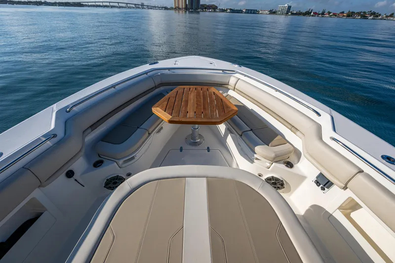Slide: The Image of 2024 Boston Whaler 380 Outrage boat interior with seating and wooden table on calm water. - 23
