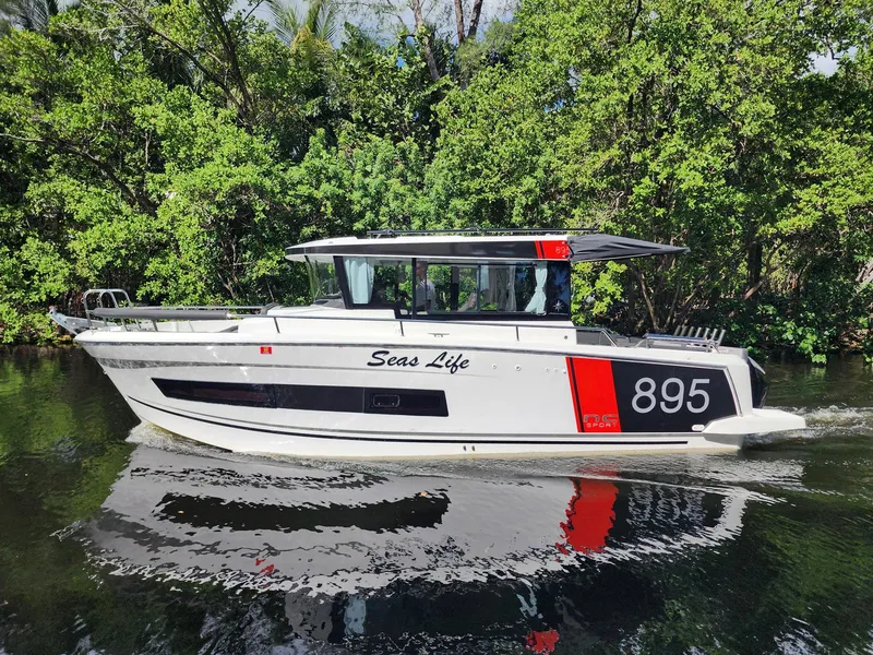 Slide: The Image of 2023 Jeanneau NC Sport 895 boat cruising on a calm river, surrounded by lush greenery. - 1