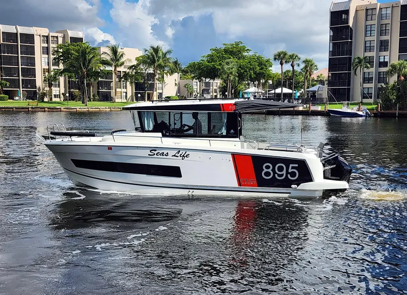 Slide: The Image of 2023 Jeanneau NC Sport 895 boat cruising on a sunny day near waterfront buildings. - 2