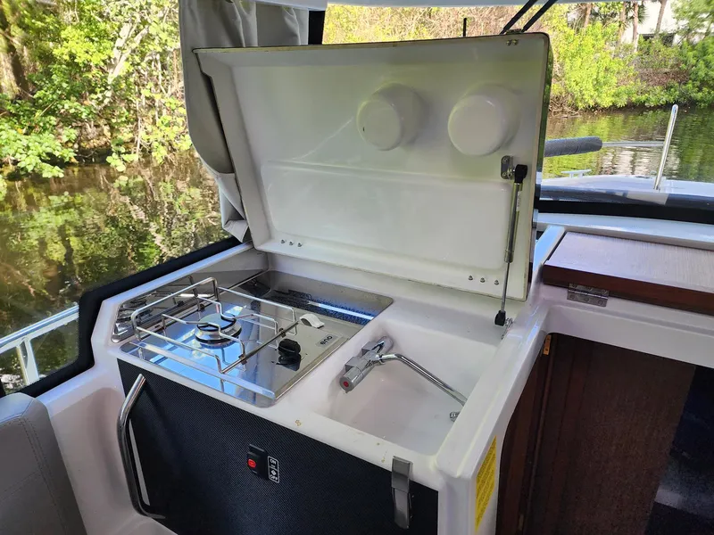 Slide: The Image of 2023 Jeanneau NC Sport 895 boat kitchen with stove and sink, near a scenic waterway. - 28