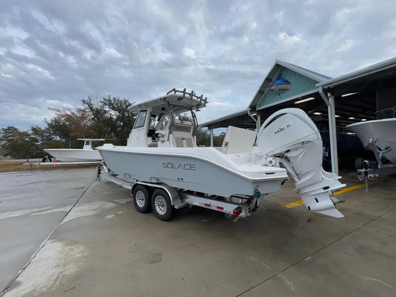 Slide: The Image of 2025 Solace 28 HCS boat on trailer, parked outside a marina under cloudy skies. - 21