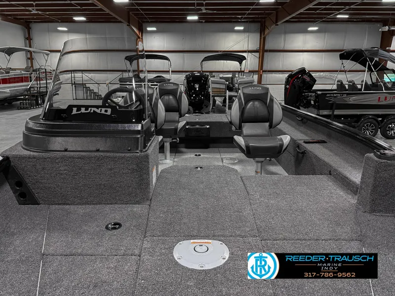 Slide: The Image of 2025 Lund 1775 Impact XS Single boat interior in showroom, featuring seating and steering console. - 17