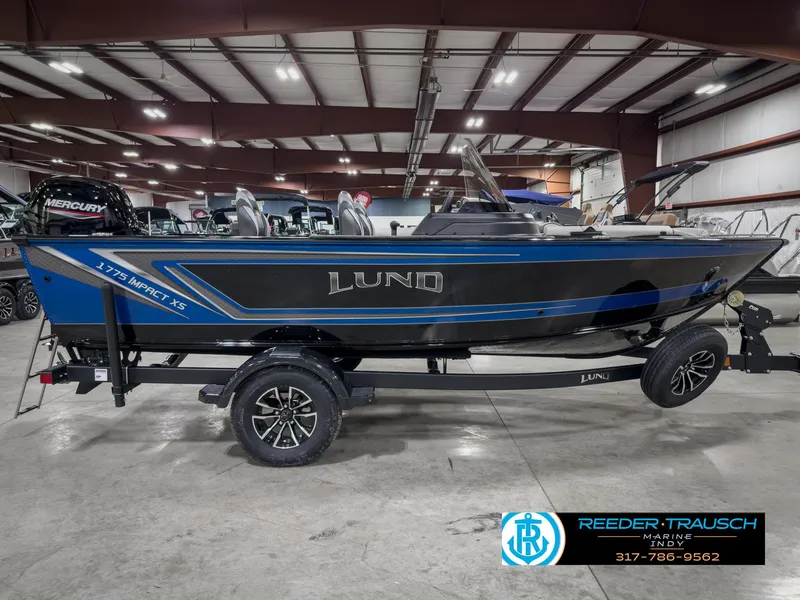 Slide: The Image of 2025 Lund 1775 IMPACT XS boat in showroom, black and blue design, on trailer. - 5