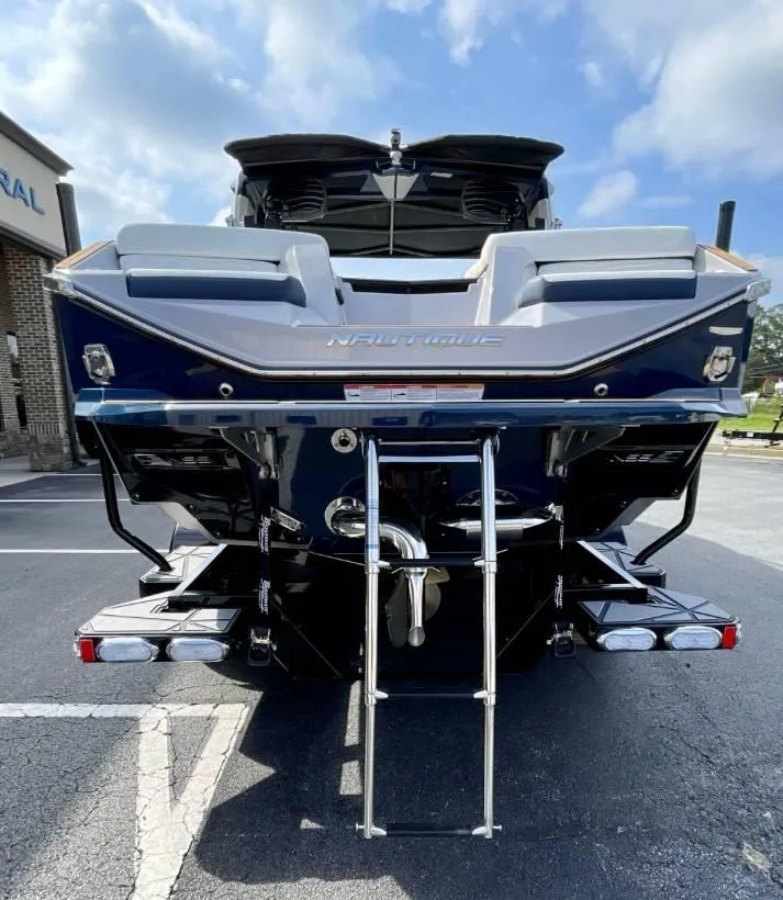 Slide: The Image of 2025 Nautique G23 boat rear view with ladder, parked outdoors under a blue sky. - 22