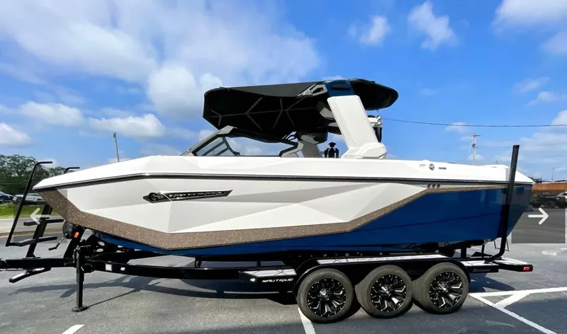 Slide: The Image of 2025 Nautique G23 boat on trailer, white and blue design, parked outdoors under blue sky. - 4